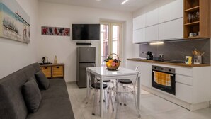 A modern kitchen with white cabinets, a built-in oven, and a dining area with a glass table and chairs. - ZenOrlando House Apartament Sea view+Parking 2S (Taormina)