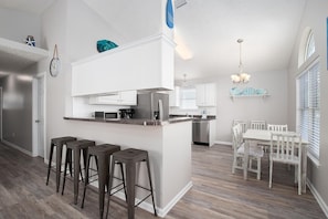 Een moderne keuken met een centraal eiland, barstoelen en een eethoek met een witte tafel en stoelen.