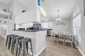Una cocina moderna con armarios blancos, una isla central con taburetes y un comedor con mesa y sillas de madera.