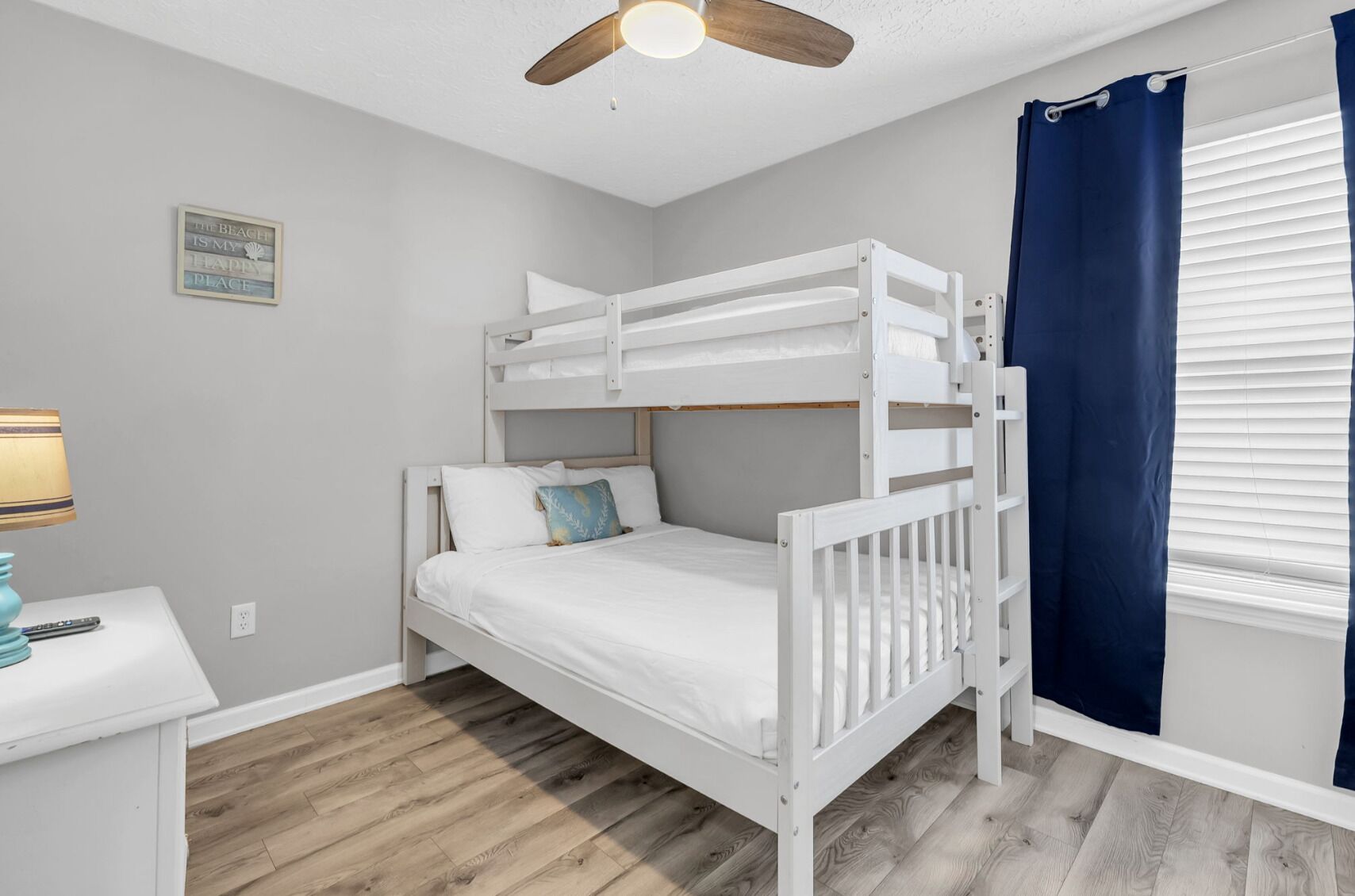 Habitación con literas, ventilador de techo, mesita de noche con lámpara y ventana con cortinas.