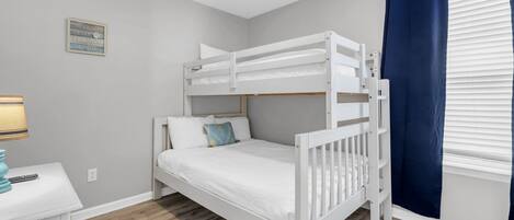 Habitación con literas, ventilador de techo, mesita de noche con lámpara y ventana con cortinas.