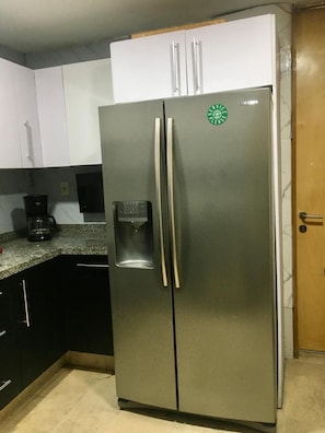 Ein Edelstahl-Kühlschrank mit Wasserspender, eine Kaffeemaschine auf der Arbeitsplatte und eine Holztür.