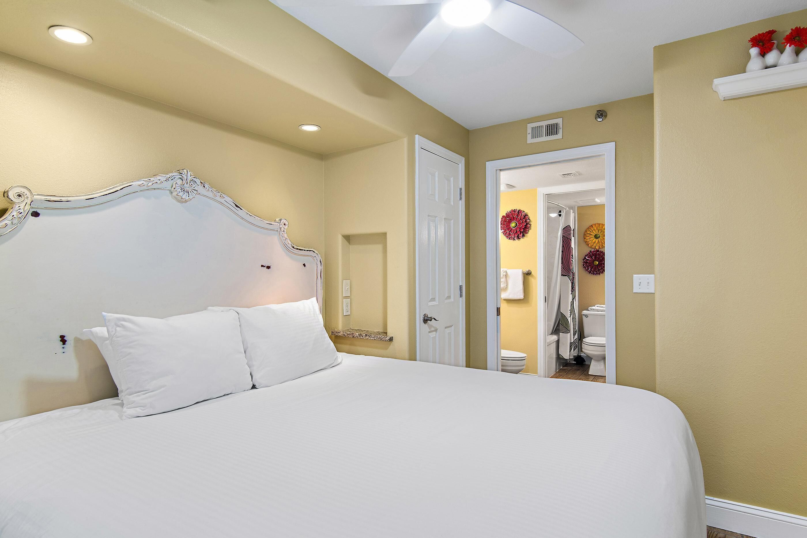 A hotel room with a large bed, a white headboard, and a door leading to a bathroom.