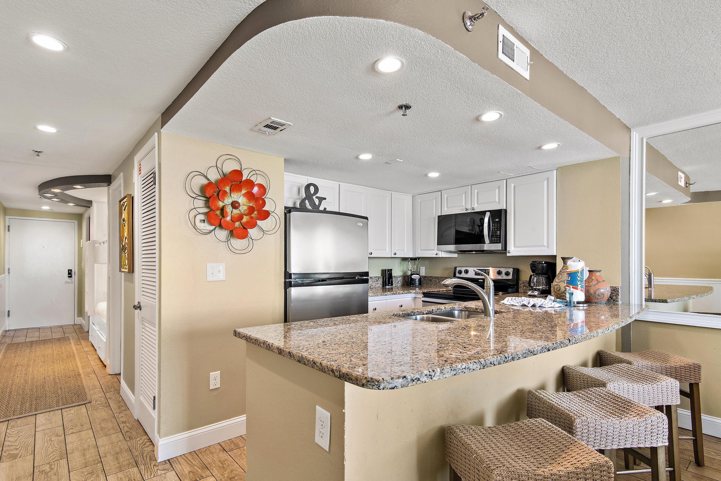 A kitchen with white cabinets, a granite countertop, and a stainless steel refrigerator.