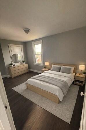 Een slaapkamer met een bed, een dressoir, nachtkastjes en een raam.