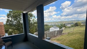 Ein überdachter Außenbereich mit einer Bank, Blick auf eine Rasenfläche und eine entfernte Brücke.