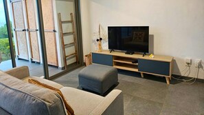 A modern living room with a sofa, a TV on a wooden stand, and a sliding glass door leading to an outdoor area.
