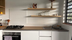 A kitchen with white cabinets, a gas stove, a sink, and wooden shelves with jars and a sculpture.