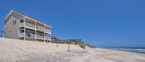 Ein Strandhaus mit Balkon und einer Treppe zum Strand, mit freiem Blick auf den Ozean.
