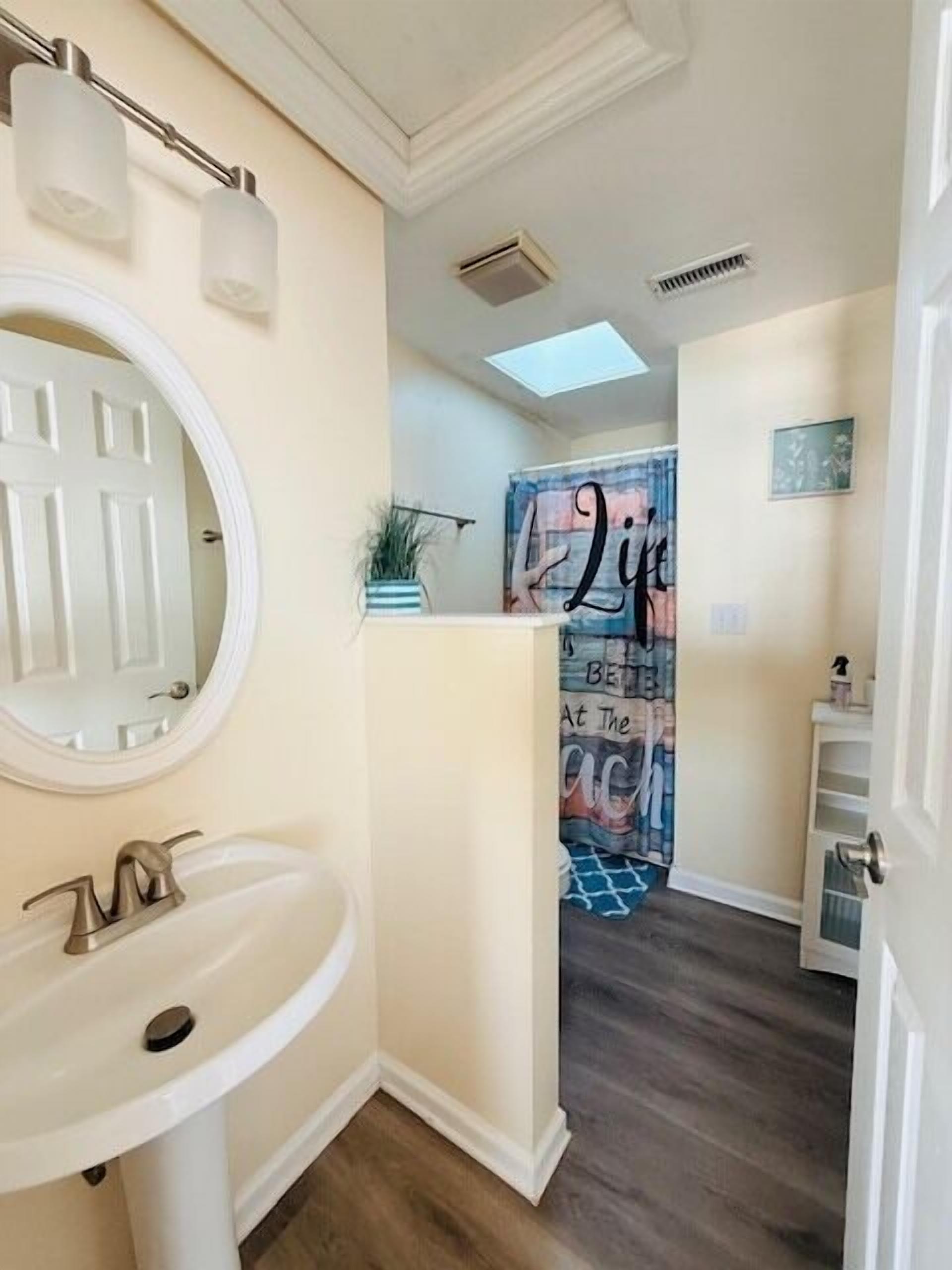 Une salle de bain avec un lavabo blanc, un miroir et un luminaire au plafond.