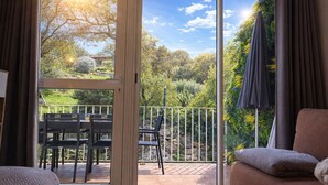 En balkon med et bord og stole, udsigt til grøn vegetation og træer, og en klar himmel.