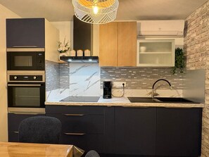 A modern kitchen with built-in appliances, a marble backsplash, and a brick accent wall. - Appartement rénové pour 6 pers tout équipé dans résidence piscine & mer (serra di ferro)