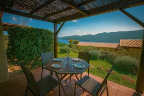 A covered outdoor dining area with a table set for two, overlooking a scenic landscape with mountains and a body of water. - Mini villa vue mer et wifi dans petite résidence*** avec piscine chauffée (Serra-di-Ferro)