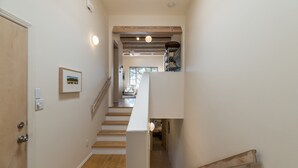 Un escalier avec des marches en bois menant à un palier, une porte blanche sur la gauche et un tableau encadré au mur.