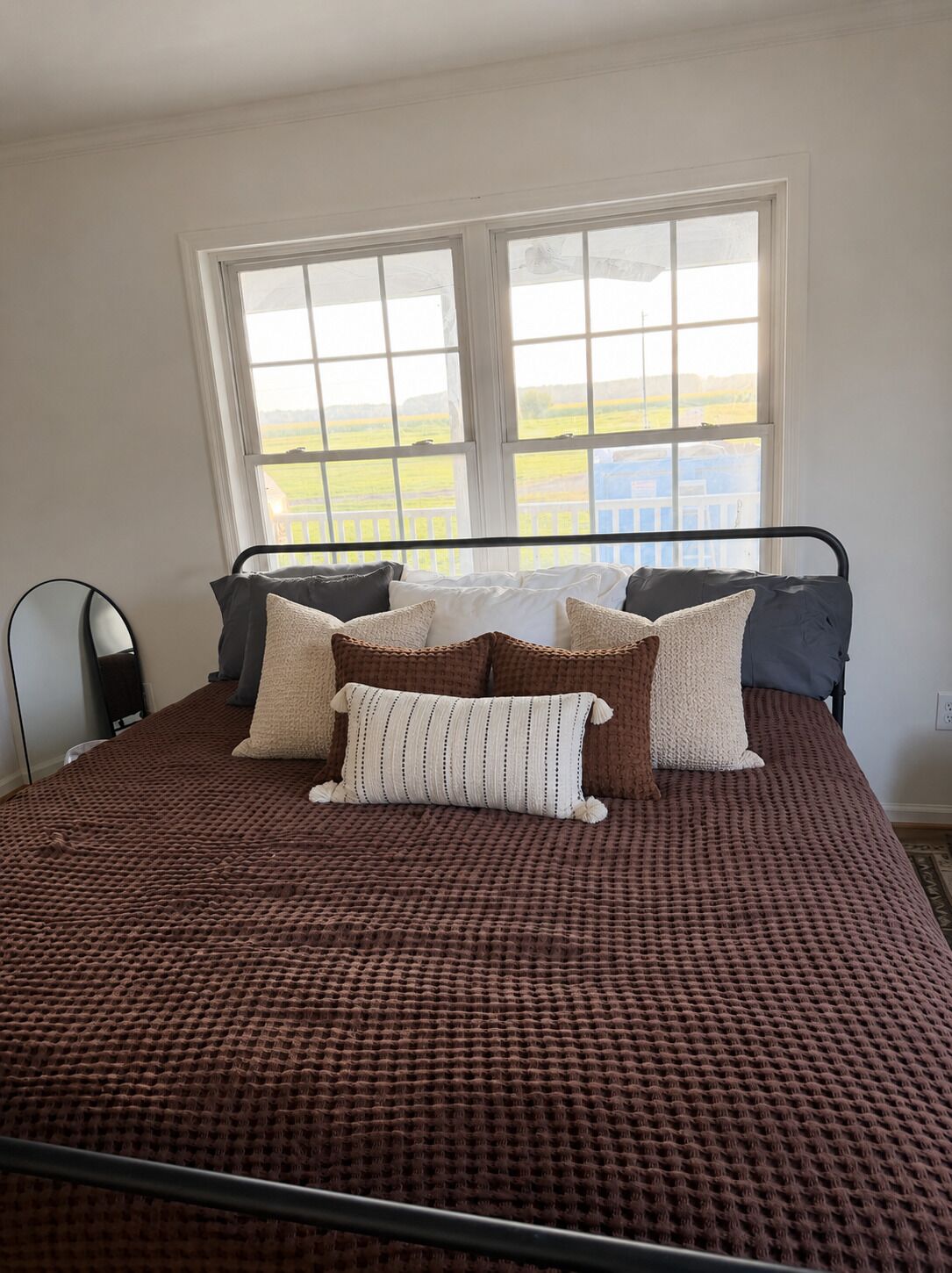 A bed with a brown textured bedspread, a metal frame, and multiple pillows.