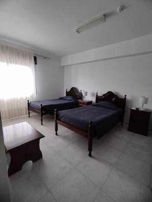 Ein Zimmer mit zwei Holzbett, einem kleinen Tisch und einer Deckenleuchte.
