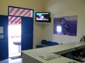 A room with a desk, chairs, a television, and a painting on the wall. - Hospedaria Jsf (Horta)