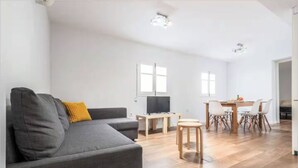 A living room with a grey sofa, a wooden dining table with chairs, and a TV. - Home2Book Family Stay Near Seville Center (Seville)