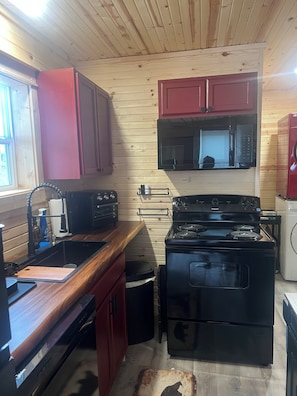 Una cocina pequeña con paredes de madera, estufa, microondas y armarios rojos.
