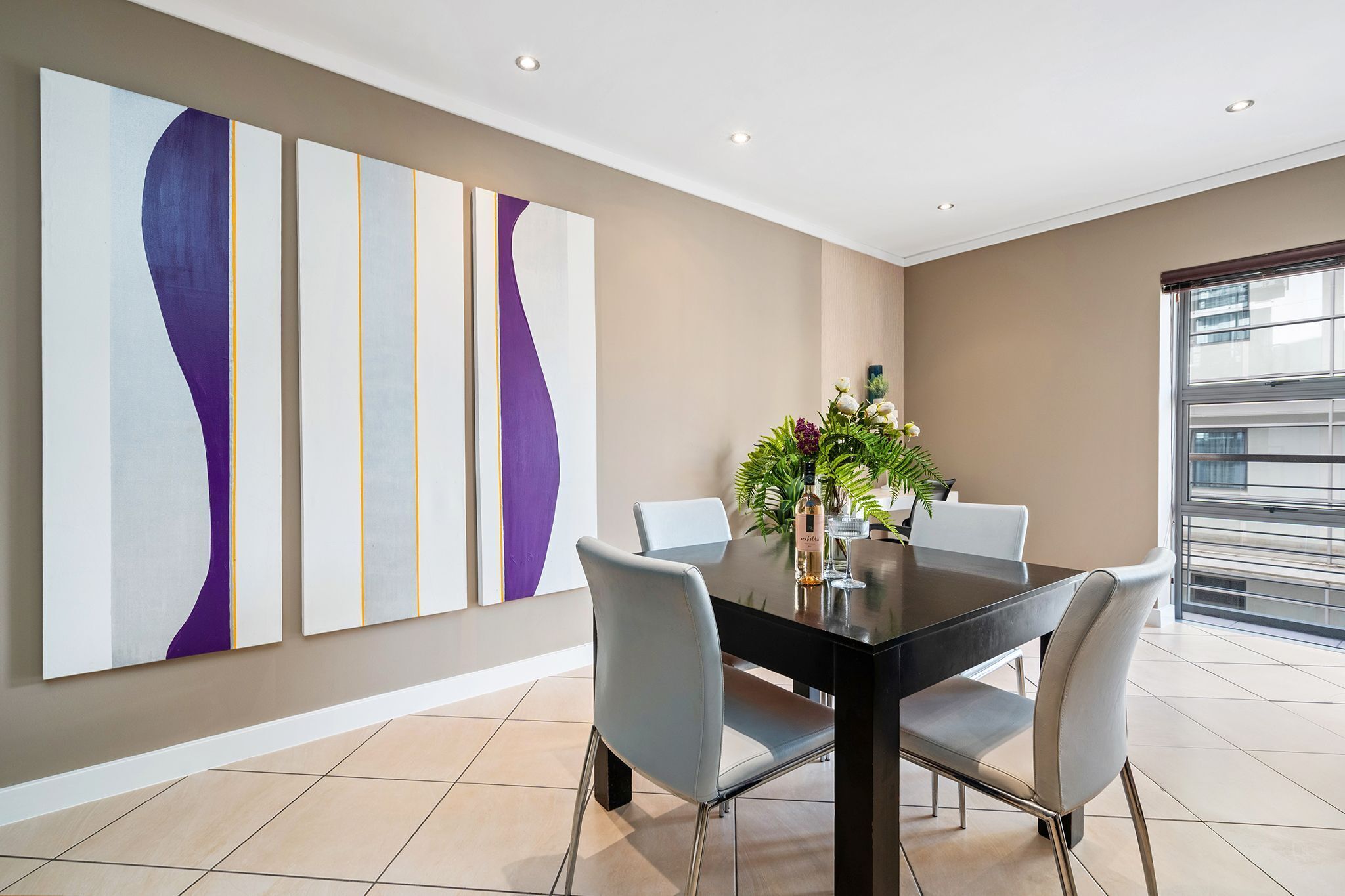 A modern dining area with a black table, grey chairs, and abstract wall art.