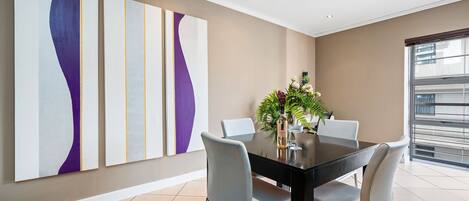 A modern dining area with a black table, grey chairs, and abstract wall art.