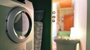 Une machine à laver à chargement frontal se trouve dans une pièce où il y a un lit et une table de chevet.