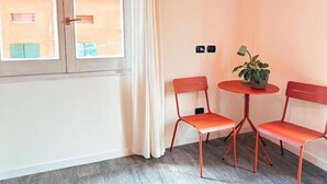 Une pièce avec une fenêtre, deux chaises rouges, une petite table ronde avec une plante et un rideau.
