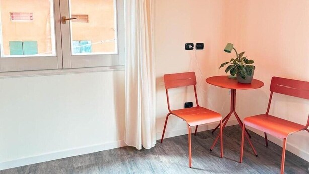 Une pièce avec une fenêtre, deux chaises rouges, une petite table ronde avec une plante et un rideau.