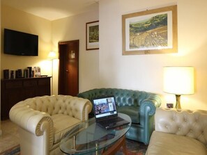 Ein Hotelzimmer mit einem Glastisch, zwei gepolsterten Sesseln, einem grünen Sofa, einem Flachbildfernseher und einem Bild an der Wand.