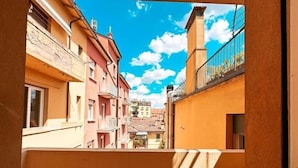 Une ruelle étroite entre deux immeubles dotés de balcons, un ciel dégagé et une vue lointaine d’un bâtiment surmonté d’un dôme.