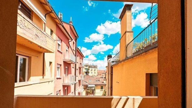 Une ruelle étroite entre deux immeubles dotés de balcons, un ciel dégagé et une vue lointaine d’un bâtiment surmonté d’un dôme.