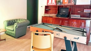 Une table de billard avec une queue de billard, un canapé vert et un meuble en bois orné de tableaux encadrés.