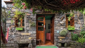 A stone building with a wooden door, potted plants, and a green mat at the entrance. - Casa Belo Jardim - Studio with garden (Arco da Calheta)