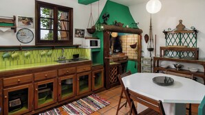 A kitchen with wooden cabinets, a green backsplash, a white countertop, and a dining area with a white table and chairs. - Casa Belo Jardim - Studio with garden (Arco da Calheta)