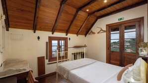 Ein Schlafzimmer mit Holzboden, einem Bett mit weißer Bettwäsche, einem Fenster mit Blick und einer Holztür.
