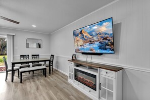 A modern living room with a flat-screen TV, fireplace, dining table, chairs, and a mirror. - Bedford Bungalow Prime DFW Location Near Everything (Bedford)