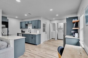 A modern kitchen with grey cabinets, a white countertop, and a wooden dining table. - Bedford Bungalow Prime DFW Location Near Everything (Bedford)