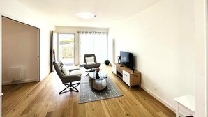 Una sala de estar con sofá, sillón, mesa de centro, televisor y puerta corredera que da a un balcón.