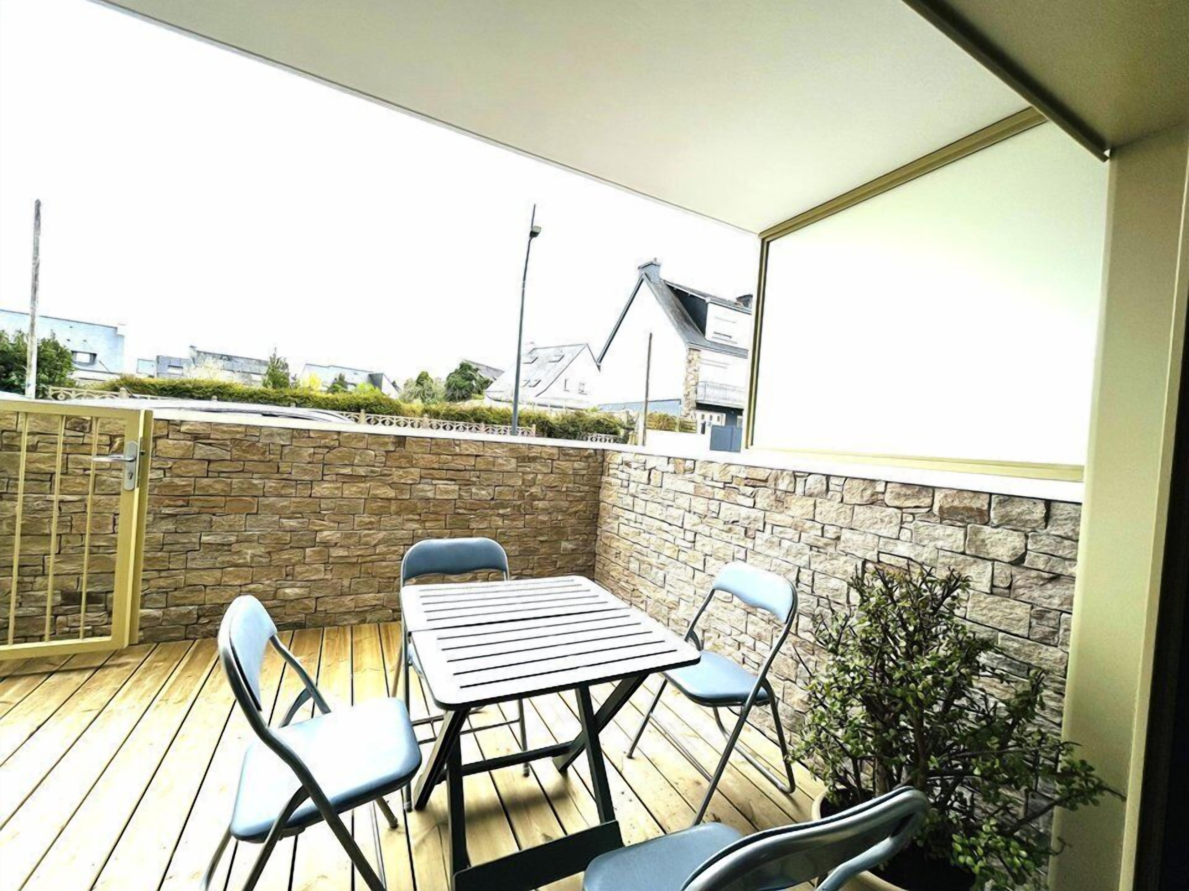 A balcony with a stone wall, a metal table, and four chairs.