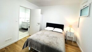 Un dormitorio con cama, mesita de noche, lámpara y baño visible a través de una puerta abierta.