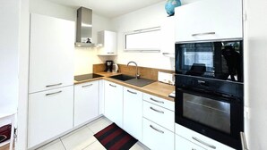 Una cocina compacta con armarios blancos, un horno negro, cafetera y ventana con vistas.