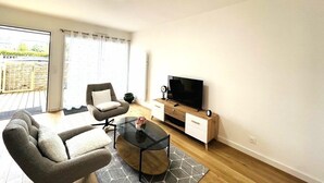 Una sala de estar moderna con sofá, sillón, mesa de centro, televisor y aparador de madera.