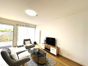 Ein modernes Wohnzimmer mit Sofa, Sesseln, Couchtisch, Fernseher und Holzschrank.