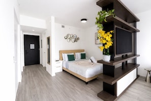 A modern bedroom with a bed, bedside tables, a TV, and a potted plant.
