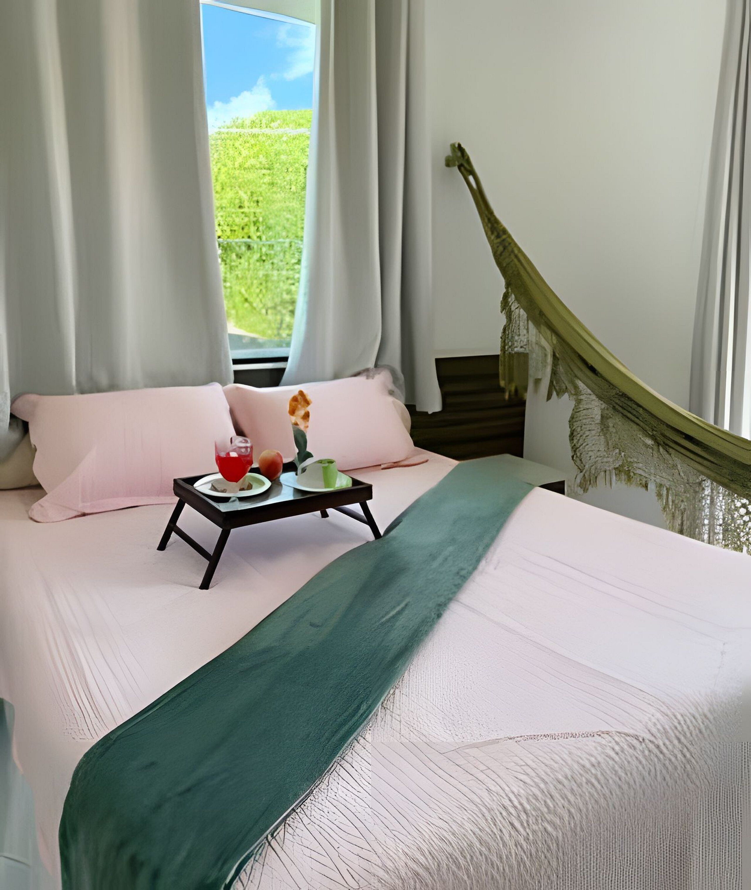 A bed with a green bedspread, two pink pillows, a tray with a glass of red drink, and a green cup.