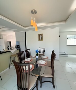 Uma área de jantar moderna com mesa de vidro, cadeiras de madeira e luminária pendente.