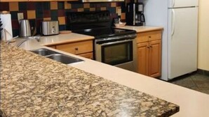 Une cuisine avec des meubles en bois, un plan de travail en granit, un four à micro-ondes, une cuisinière, un réfrigérateur et une machine à café.