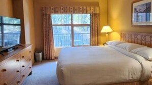 Une chambre d’hôtel avec un lit, un téléviseur posé sur une commode, une lampe et une fenêtre avec des rideaux.