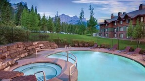 Une piscine bordée de pierres, des chaises longues et un bâtiment avec une montagne en toile de fond.