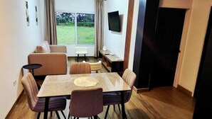 Un espace repas comprenant une table et des chaises, un canapé, un téléviseur et une fenêtre donnant sur un paysage verdoyant.